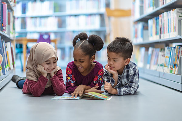 3 kids reading a book in a library